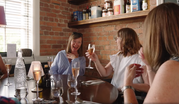 A photo of a group of women sat around a dining table laughing. 