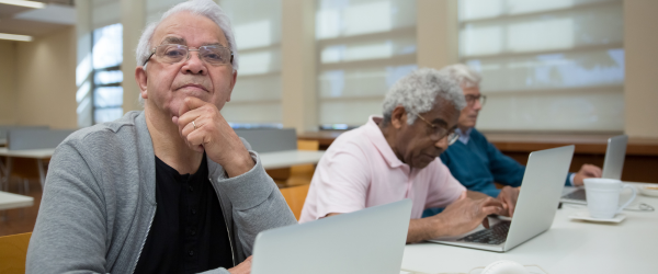 An older man on a laptop next to two other older men